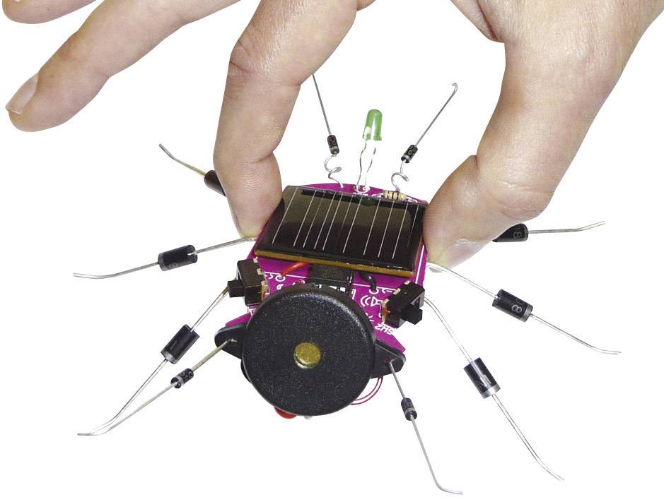 Une main tient un petit insecte robotique équipé de pattes et d'un panneau solaire. L'insecte ressemble à une araignée.