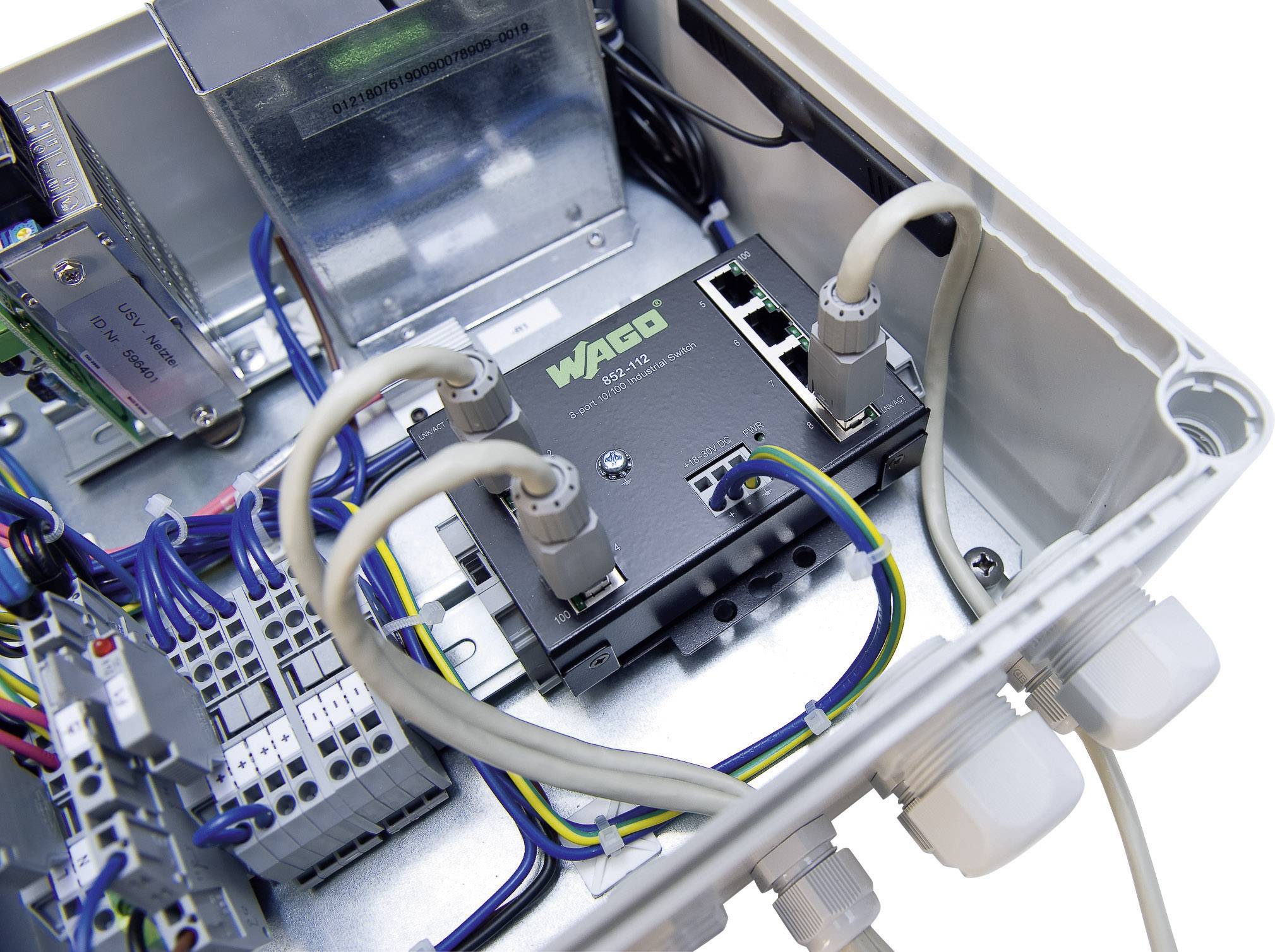 Un boîtier électronique ouvert avec un commutateur réseau de marque WAGO, relié par des câbles. Différentes connexions visibles.