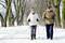 Un couple de personnes âgées marche avec des bâtons de Nordic Walking sur un chemin enneigé, entouré d'arbres.