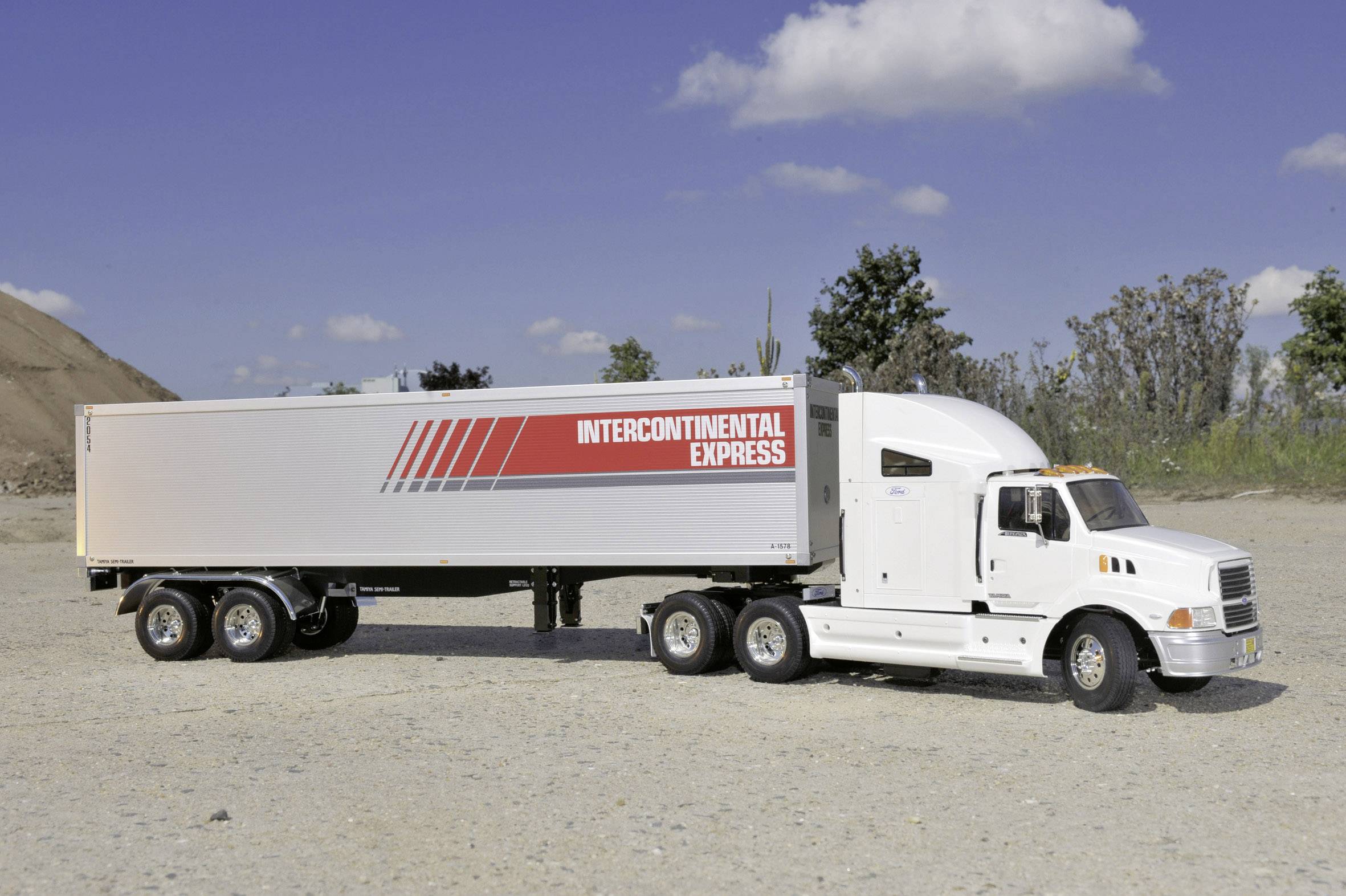 Un camion blanc avec une remorque roule sur une route. Sur la remorque est inscrit 'Intercontinental Express'. Des arbres sont visibles en arrière-plan.