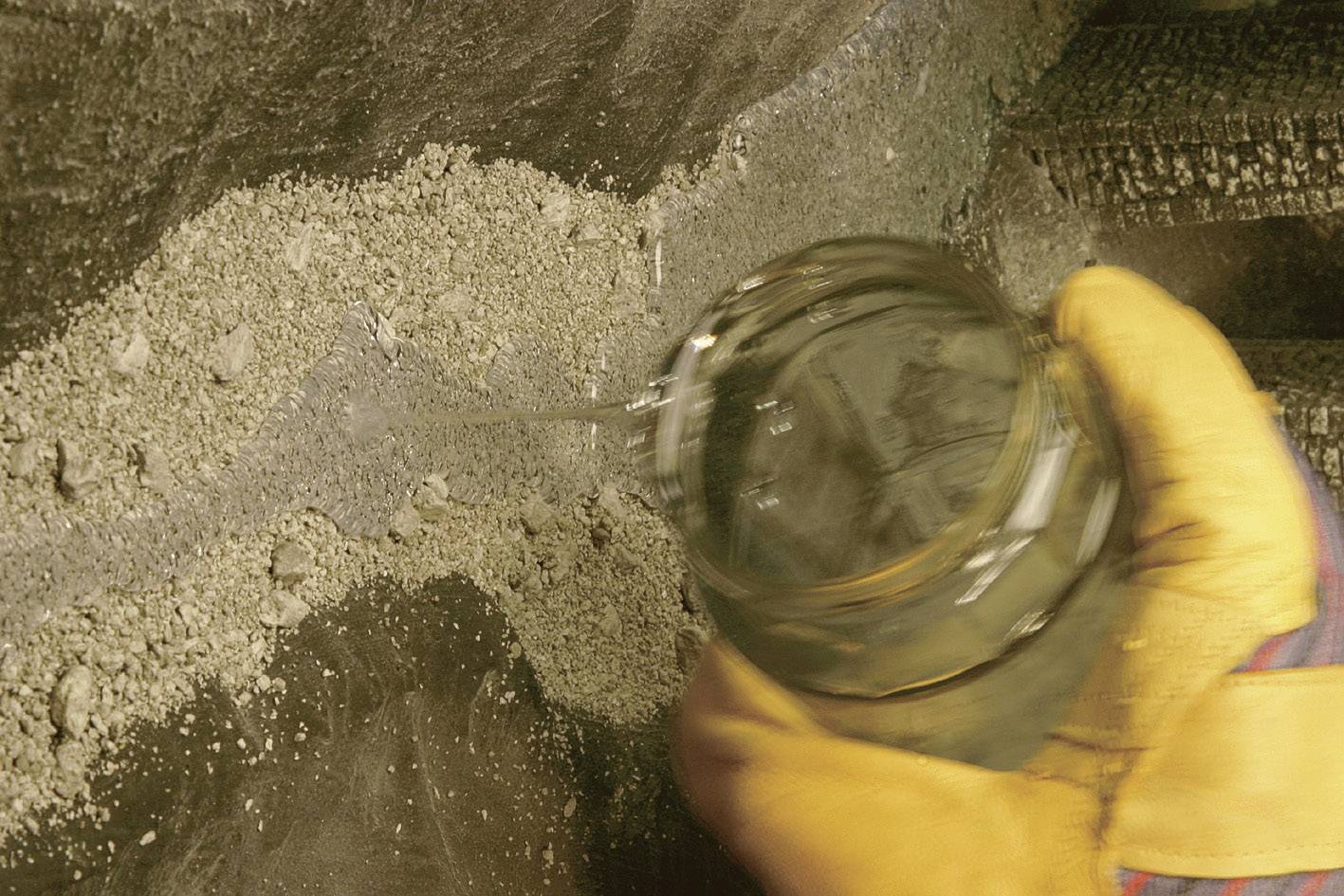 Une personne verse de l'eau d'un verre sur une surface en béton, probablement pour observer une réaction ou effectuer un nettoyage.