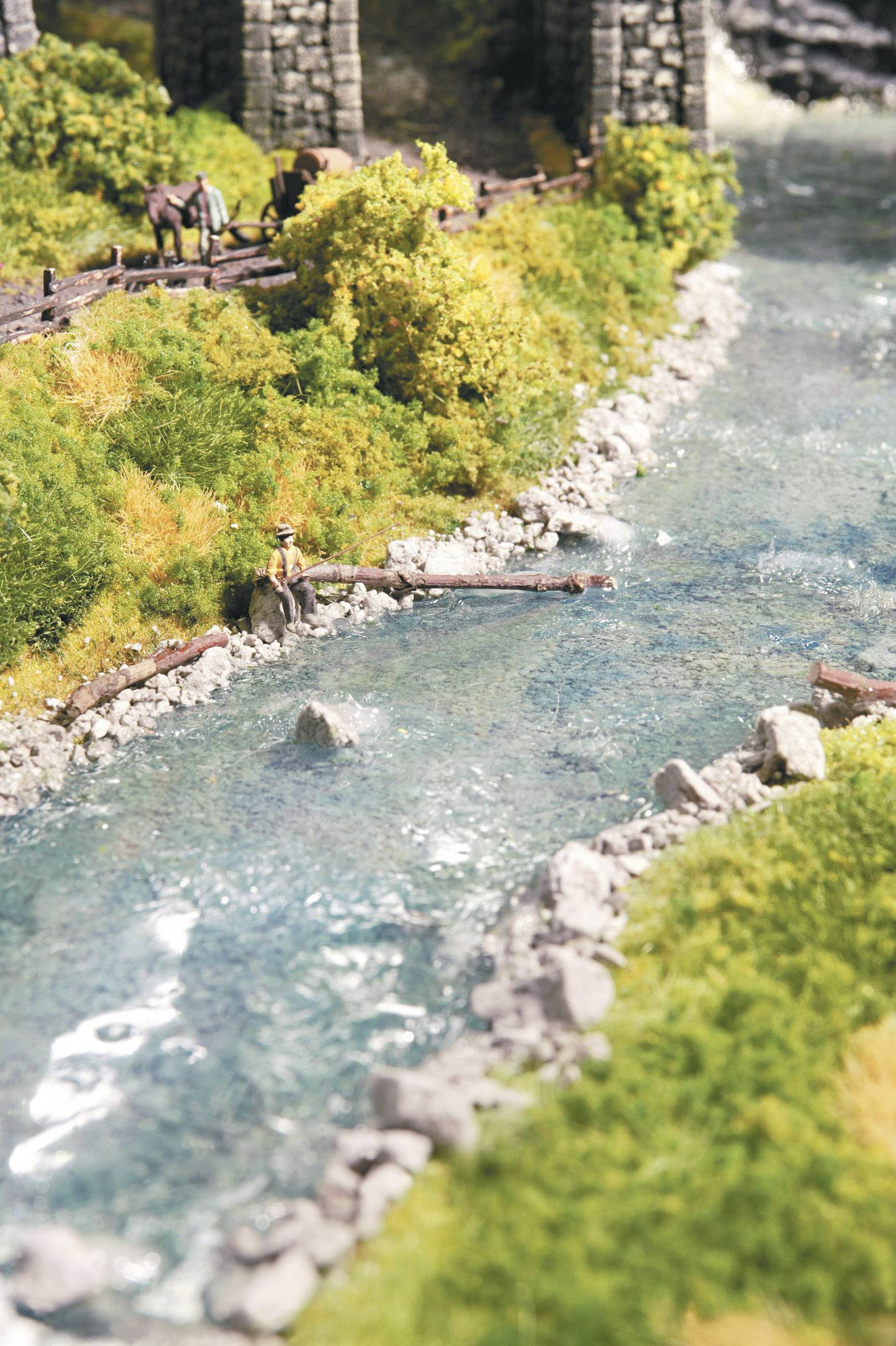Paysage modelé avec une rivière limpide, des arbres, des rochers et une figure assise sur la rive. Des chevaux se tiennent au loin près d'un pont en bois.
