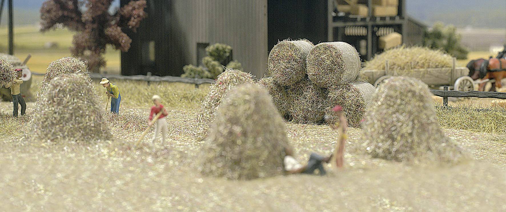 Modèle miniature d'une scène rurale avec des personnes empilant du foin et une charrette à cheval en arrière-plan.