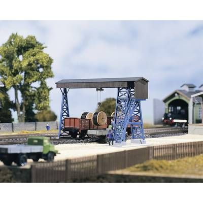 Un modèle de paysage ferroviaire représente un train de marchandises chargé de bobines de câbles, une grue et une locomotive en arrière-plan, le tout entouré d'arbres.