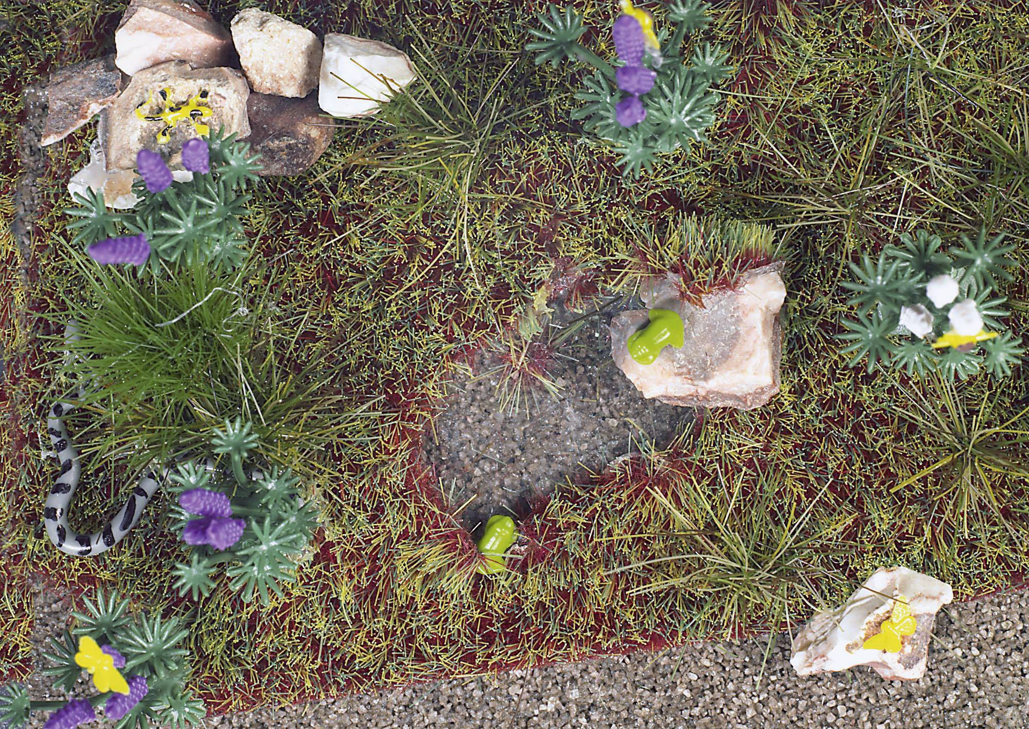 Un petit espace avec de la mousse artificielle et des plantes, comprenant des fleurs colorées et un serpent jouet qui se faufile à travers la mousse.