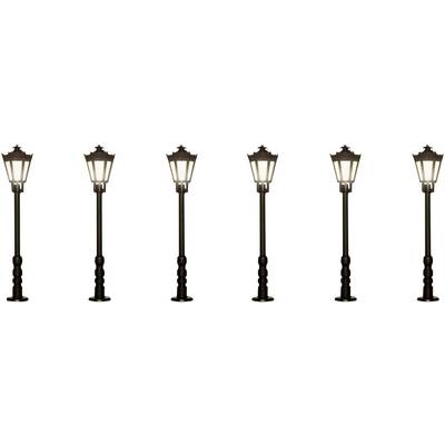 Six lanternes historiques identiques alignées, leurs ampoules illuminant la rue.