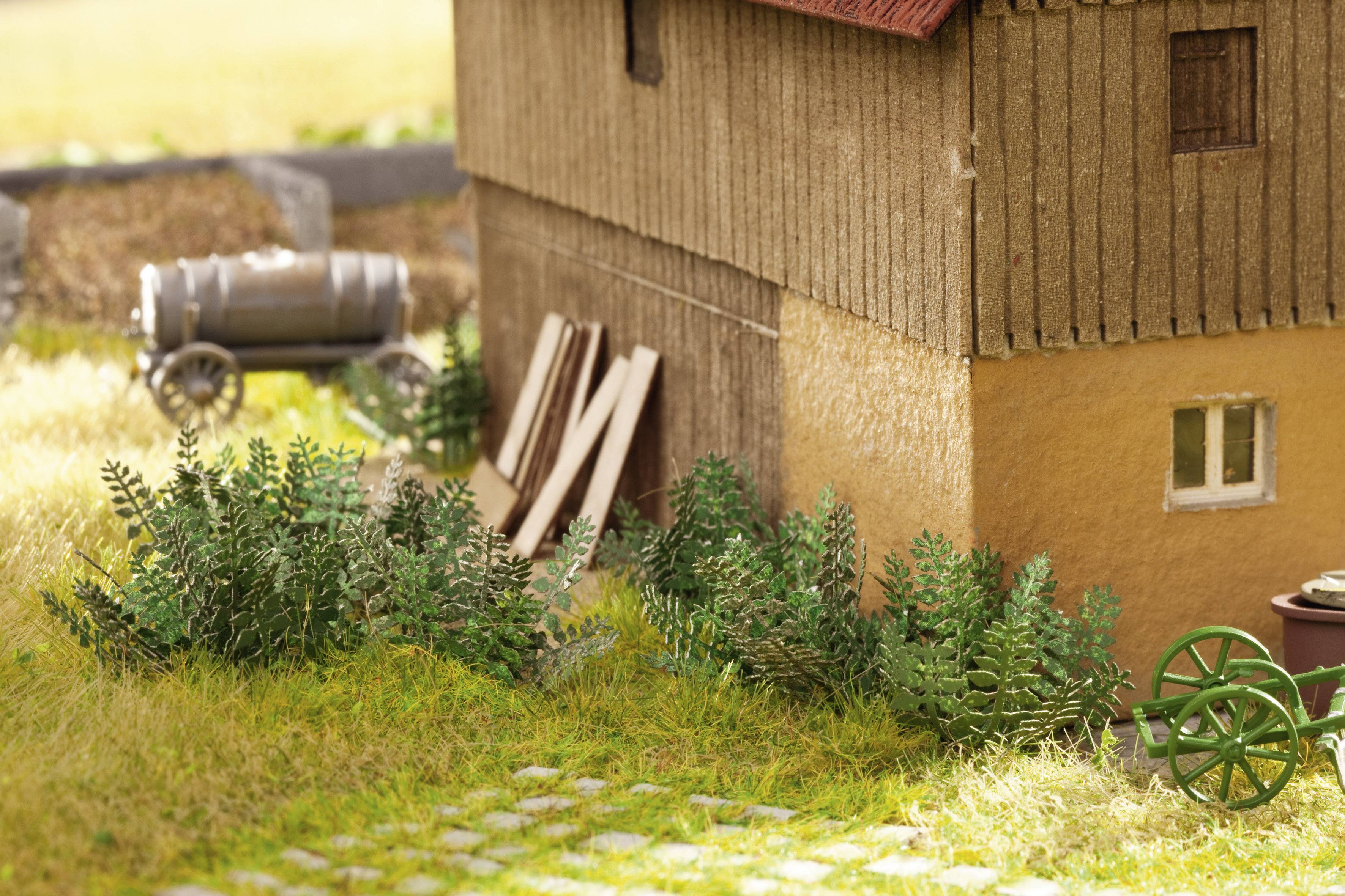 Une mini-ferme avec une grange et des planches de bois sur le côté. Au premier plan, on peut voir des buissons et une roue de chariot verte.