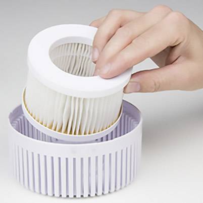Une main tient un filtre de rechange pour un purificateur d'air. Le filtre est cylindrique et possède des plis blancs destinés à la filtration des particules.