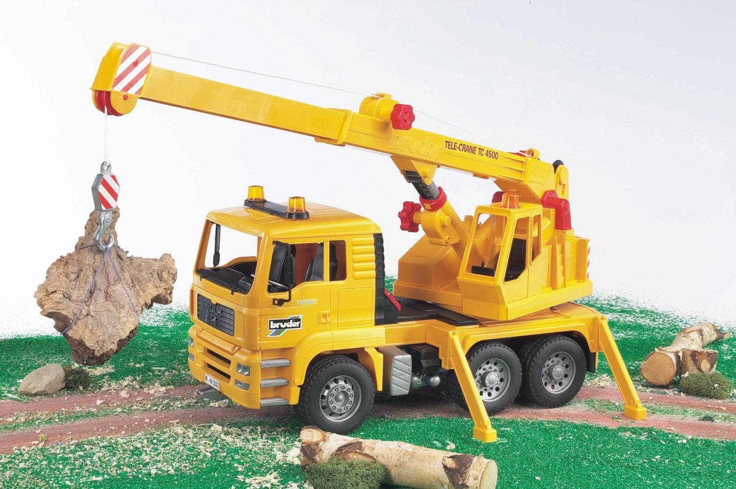 Un modèle de grue jouet jaune soulève un morceau de bois d'un fond vert. La grue est orientée vers la gauche.