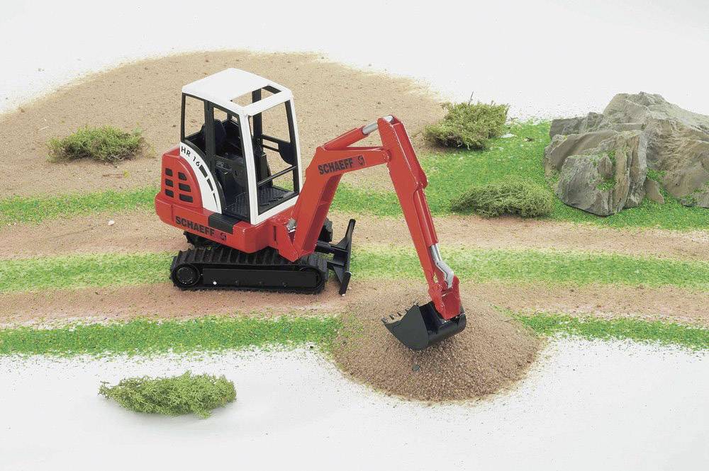 Un petit pelleteuse rouge creuse dans un paysage miniature avec de l'herbe et des rochers.