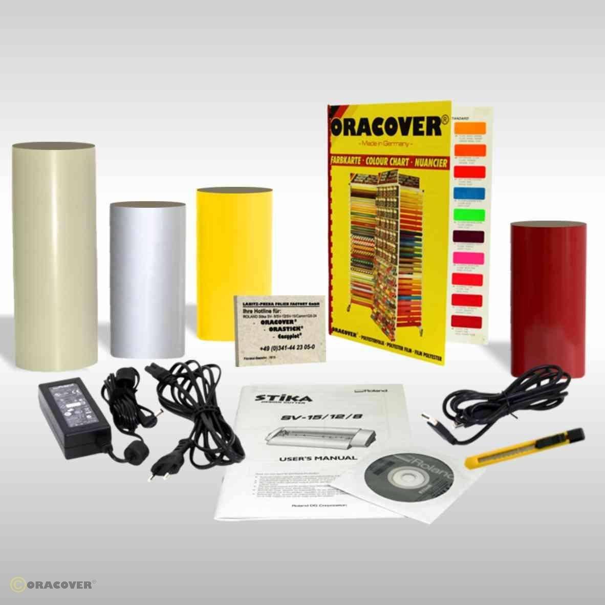 Plusieurs rouleaux de feuilles de couleur, des câbles, un bloc d'alimentation, un stylo et un manuel d'utilisation avec un CD sont disposés devant un diagramme de comparaison des couleurs.