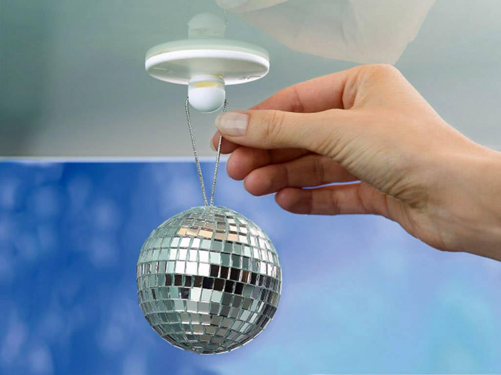 Une main accroche une petite boule disco à une fixation de plafond. L'environnement est bleu et flou, ce qui met en valeur la boule.