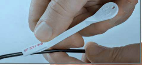 Une main tient un ruban de plastique blanc portant l'inscription « 3M 12 NE 25°F », enroulé autour d'un câble noir.