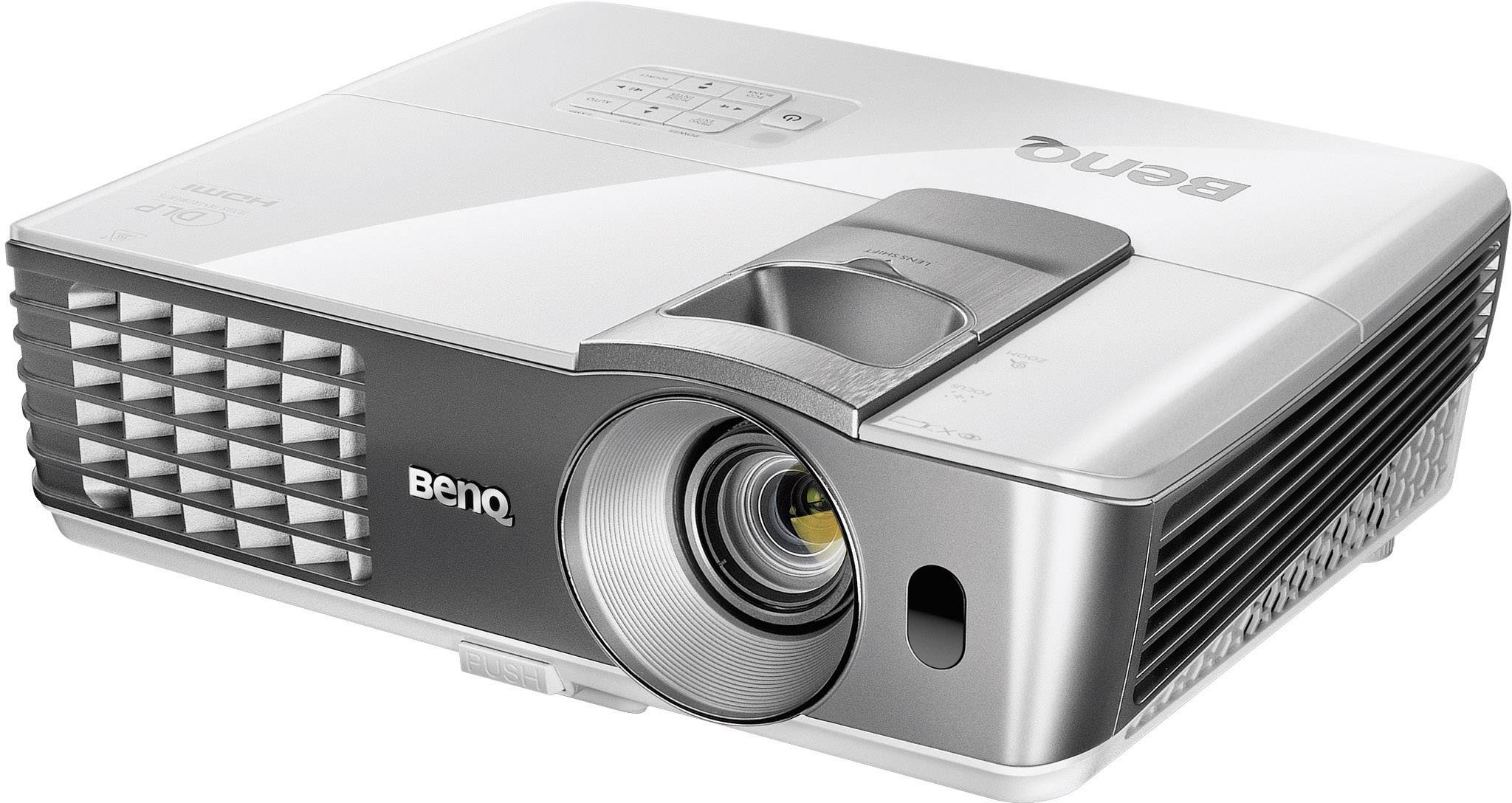 Un projecteur argenté est positionné en biais sur une table. Le logo de la marque est visible. La ventilation se trouve à gauche et l'objectif est à l'avant.