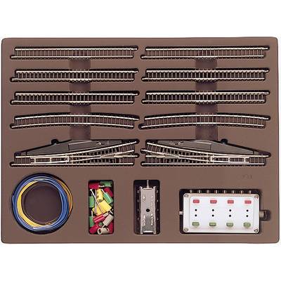 Un ensemble d'accessoires pour train miniature comprenant des rails, des fils de différentes couleurs, des connecteurs et une unité de contrôle, le tout dans un carton ouvert.