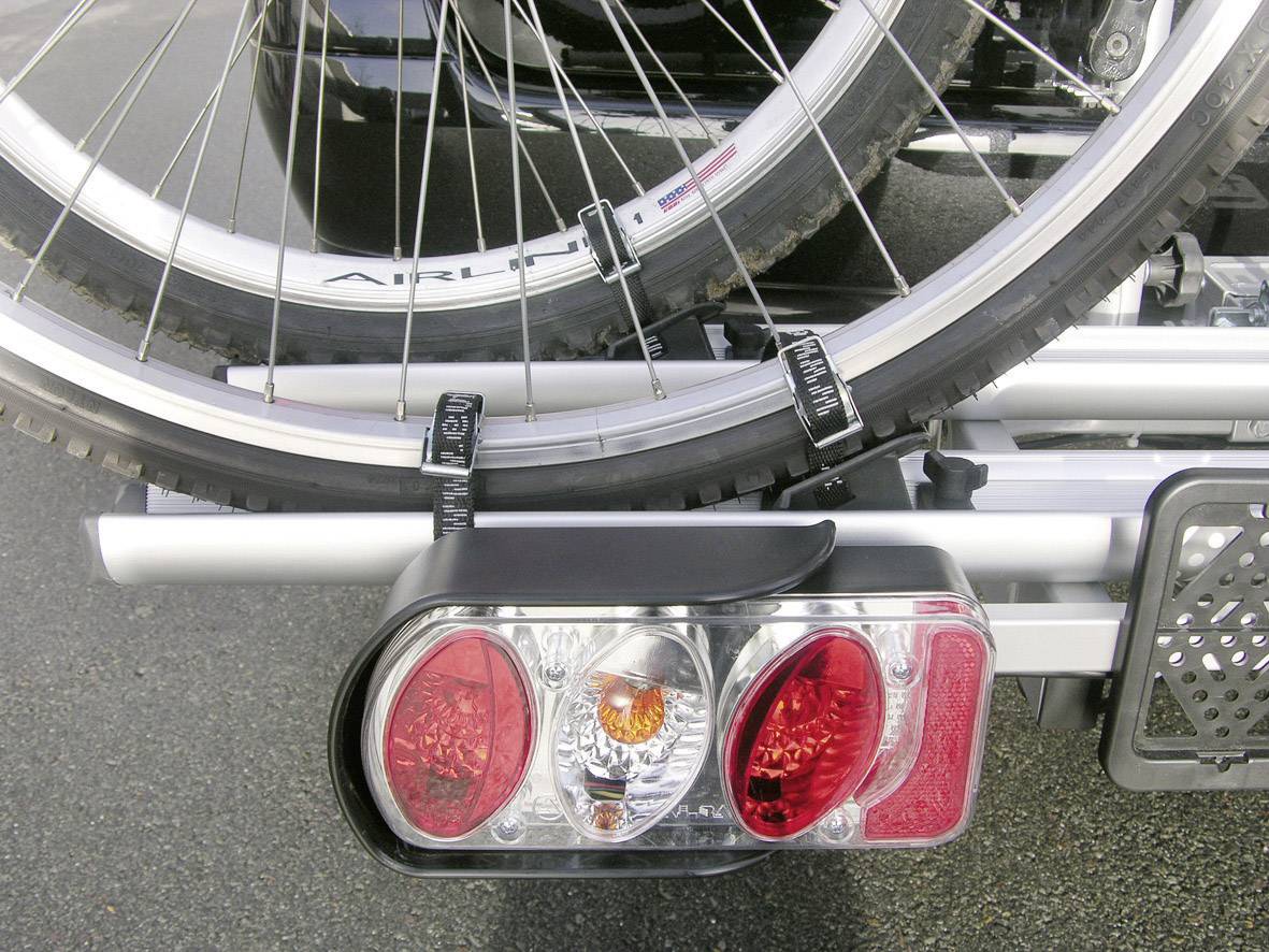 Un vélo est fixé sur un porte-vélos à l'arrière d'un véhicule. Le support est équipé de feux arrière pour la sécurité.