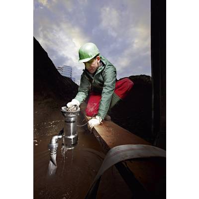 Un ouvrier portant un casque vert installe une pompe dans une zone boueuse sur un chantier de construction sous un ciel nuageux.