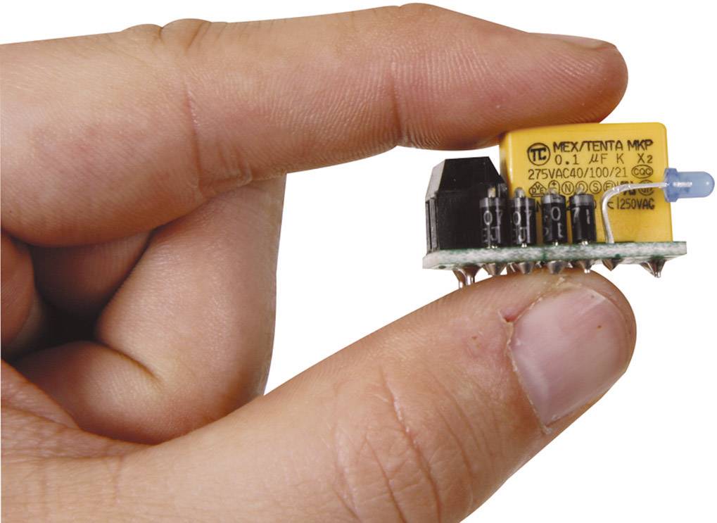 Une main tient une petite carte électronique avec un relais jaune et plusieurs composants noirs.