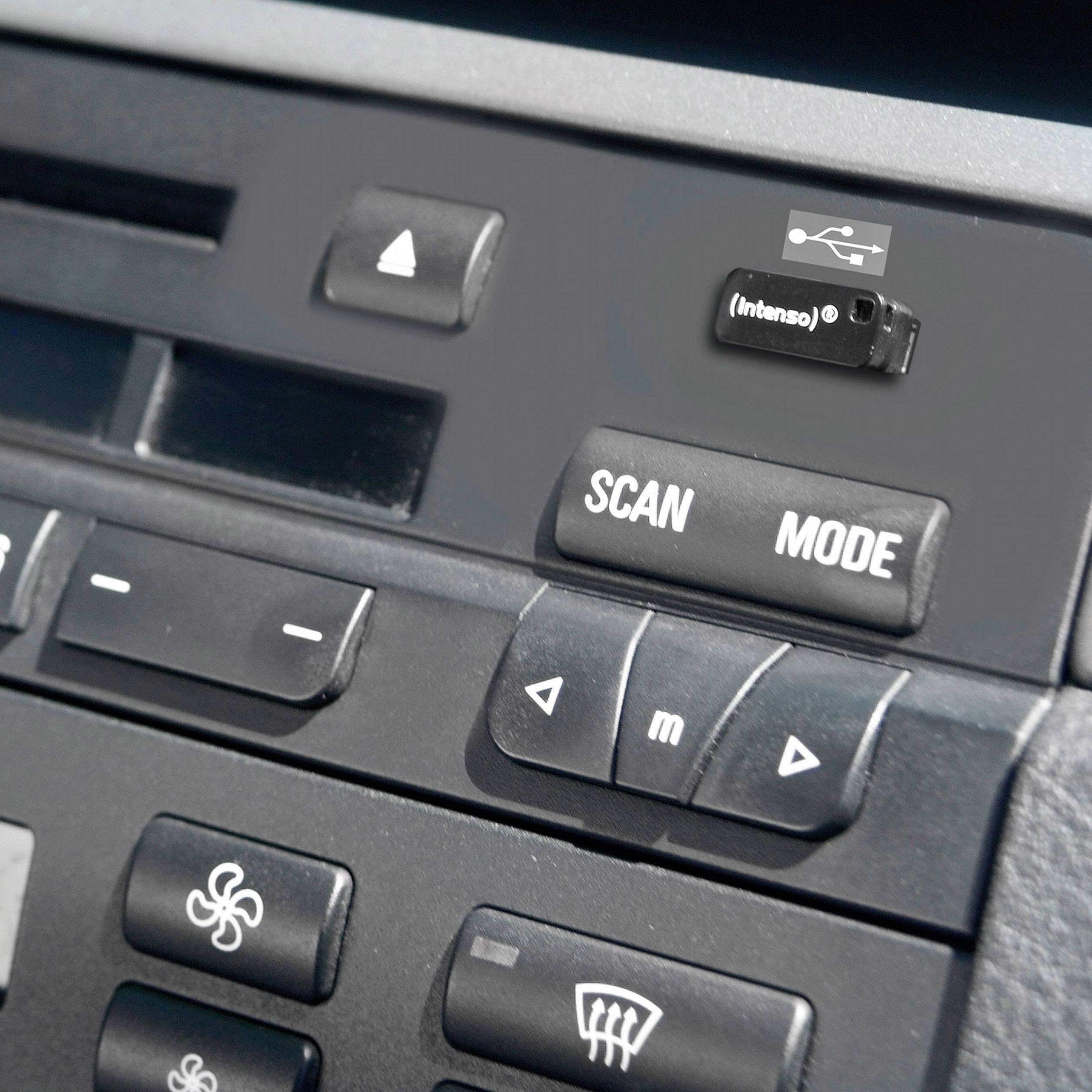 Une clé USB branchée dans la console centrale d'une voiture, près des boutons de scan et de mode, avec en dessous les commandes de ventilation.