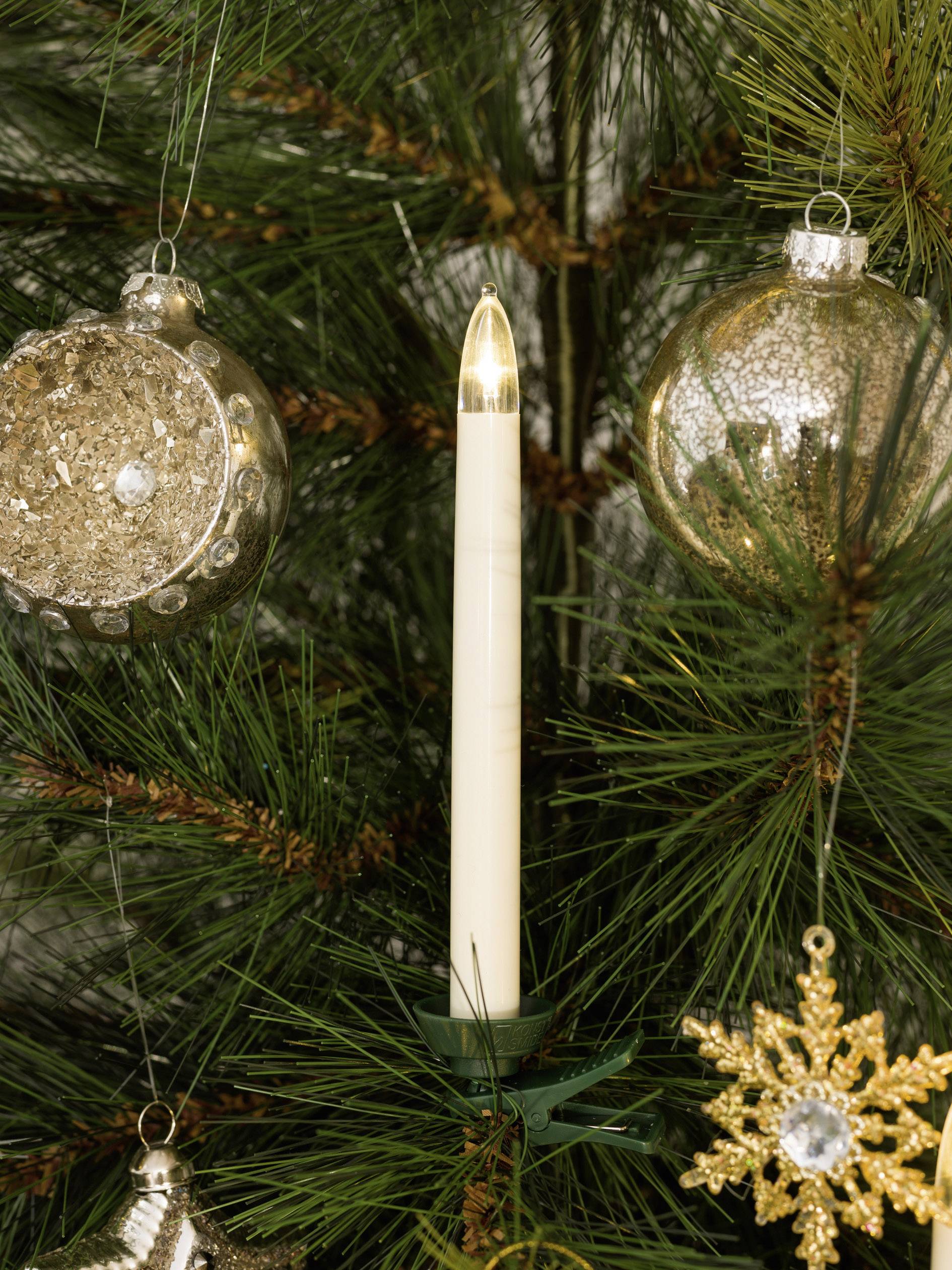 La lumière des bougies et des boules dorées sont suspendues à un sapin de Noël décoré aux branches vertes.