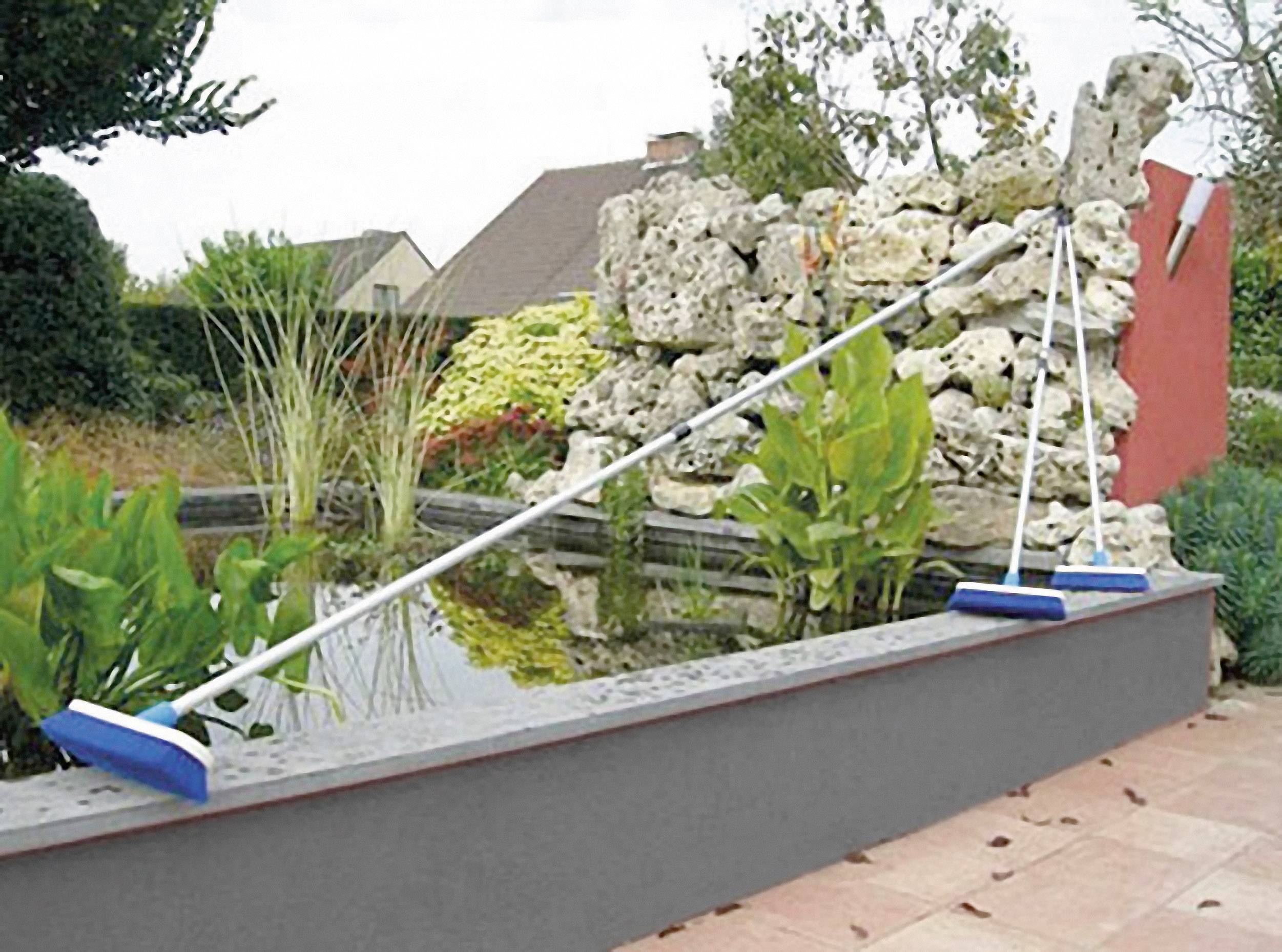 'Protection pour bordure de bassin', une tige blanche avec des extrémités bleues est placée transversalement au-dessus d'un petit bassin de jardin avec des plantes et des pierres en arrière-plan.