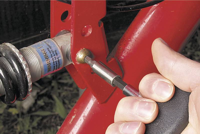 Une main serre un écrou avec une clé à six pans, fixant une pièce sur un cadre métallique rouge.