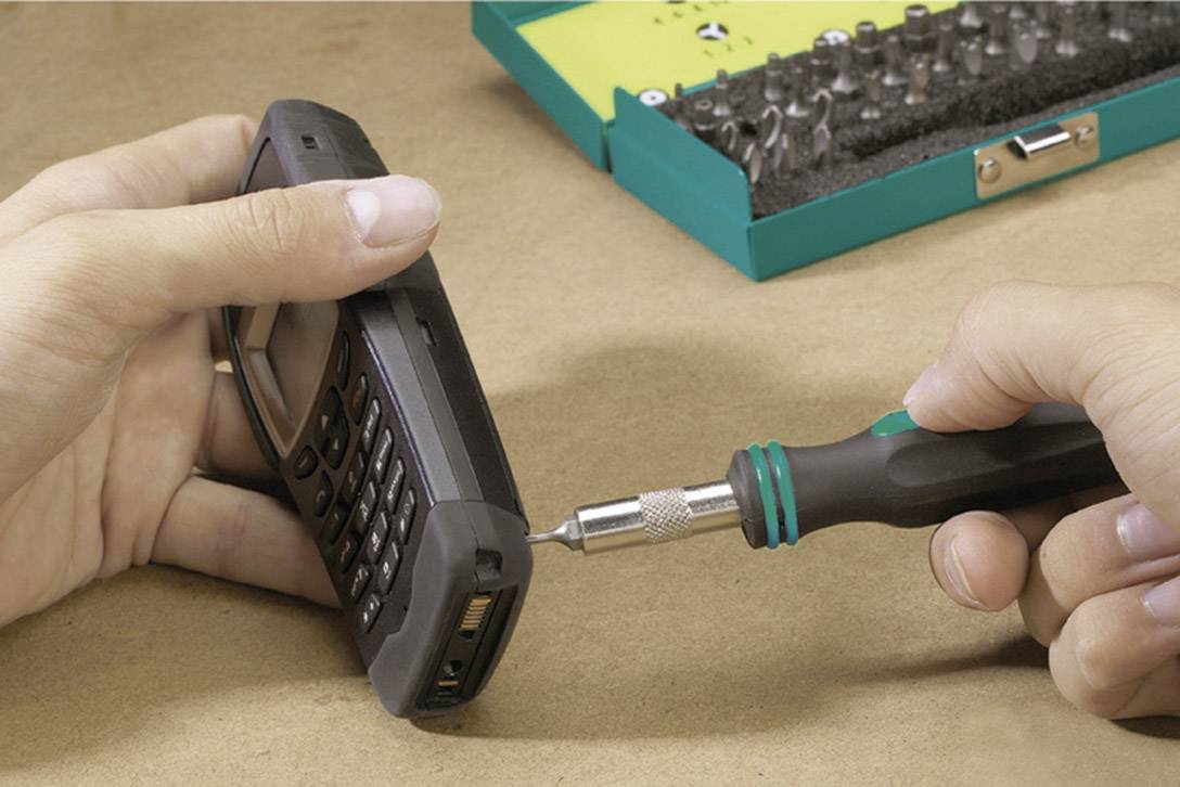 Une personne ouvre un téléphone mobile à l'aide d'un tournevis. Un coffret à outils vert est visible en arrière-plan.