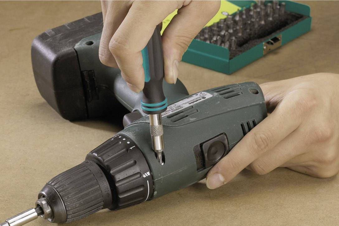 Une personne tient un tournevis et visse sur une visseuse sans fil. Un jeu d'embouts est visible en arrière-plan.