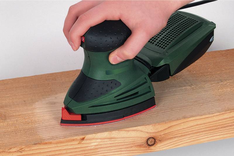 Une main utilise une ponceuse à bande verte sur une poutre en bois.