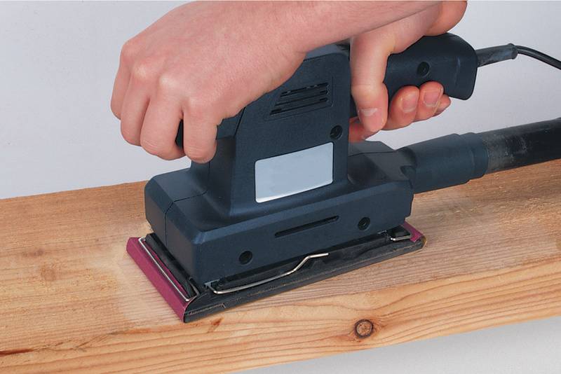 Une personne ponce une planche de bois à l'aide d'un outil de ponçage électrique.