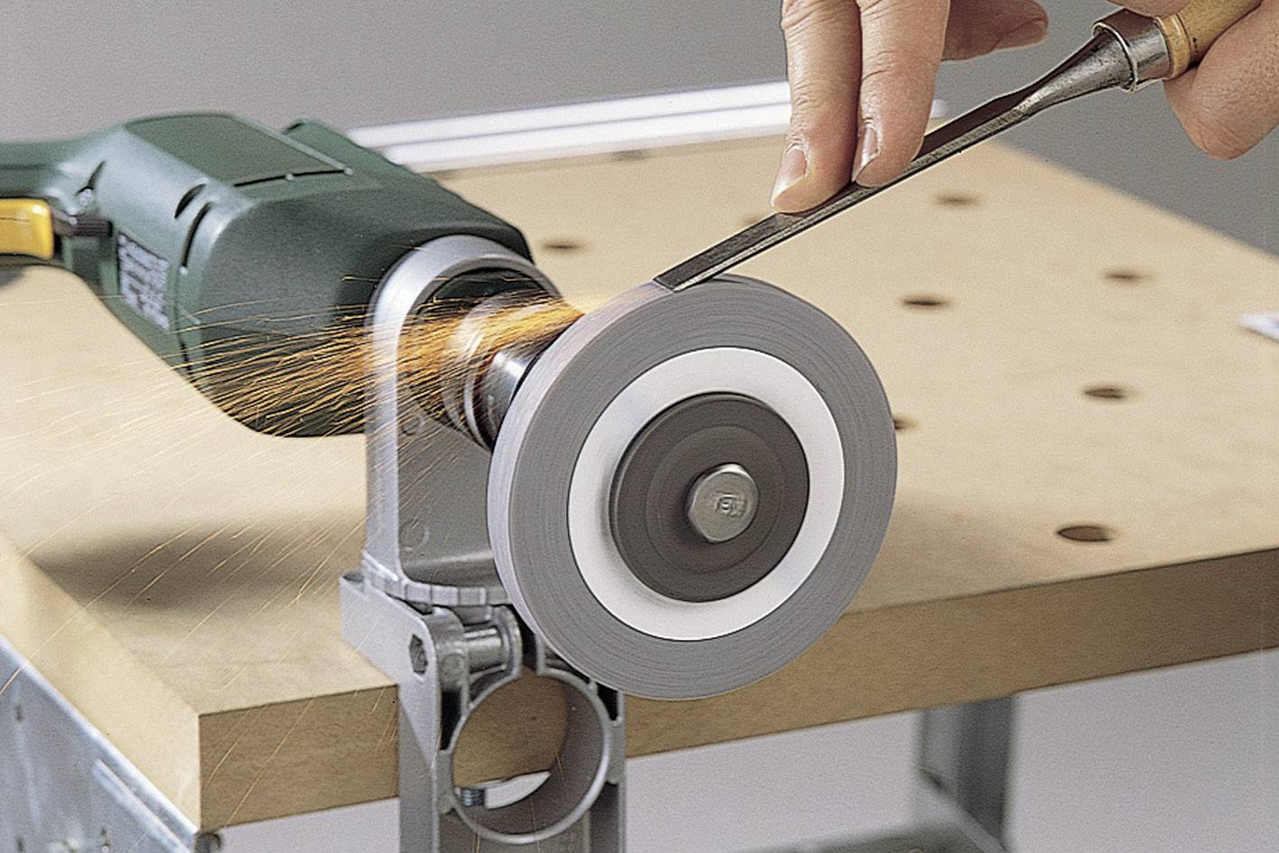 Une personne affûte un outil métallique avec un appareil de meulage électrique sur un établi. Des étincelles volent pendant le processus.