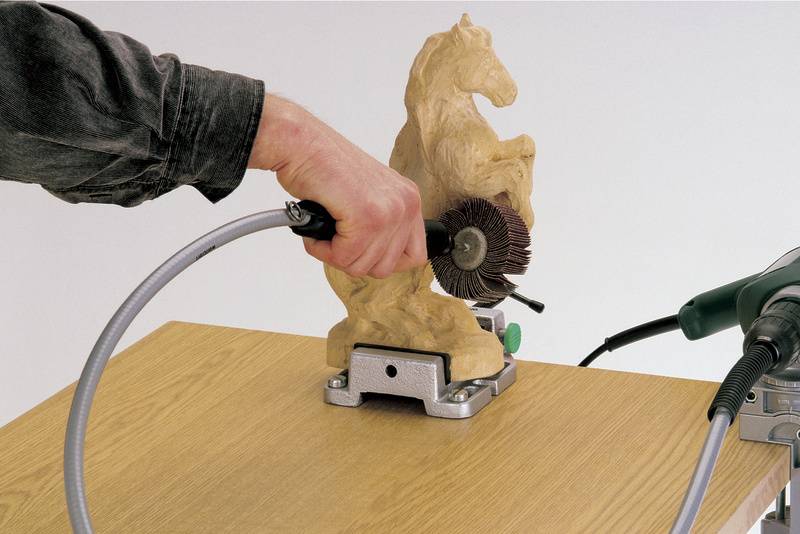 'Une personne travaille une sculpture de cheval en bois à l'aide d'une machine à poncer rotative sur une table en bois.'