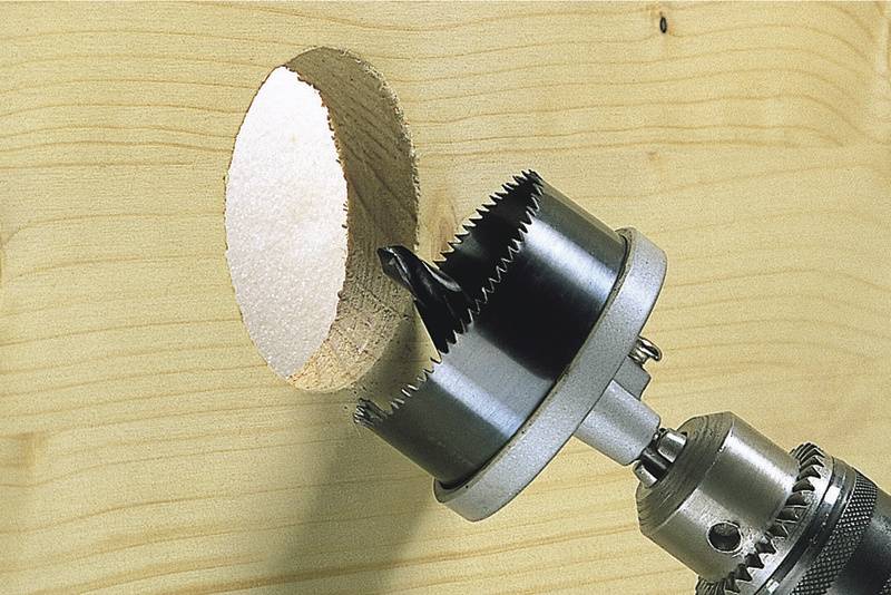 Un foret métallique perce un trou rond dans une planche en bois. Le foret a des dents tranchantes et tourne pour percer le bois de manière efficace.