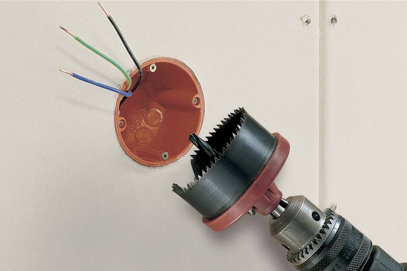 Gros plan d'une perceuse avec scie-cloche découpant un trou circulaire dans un mur pour installer une boîte électrique.