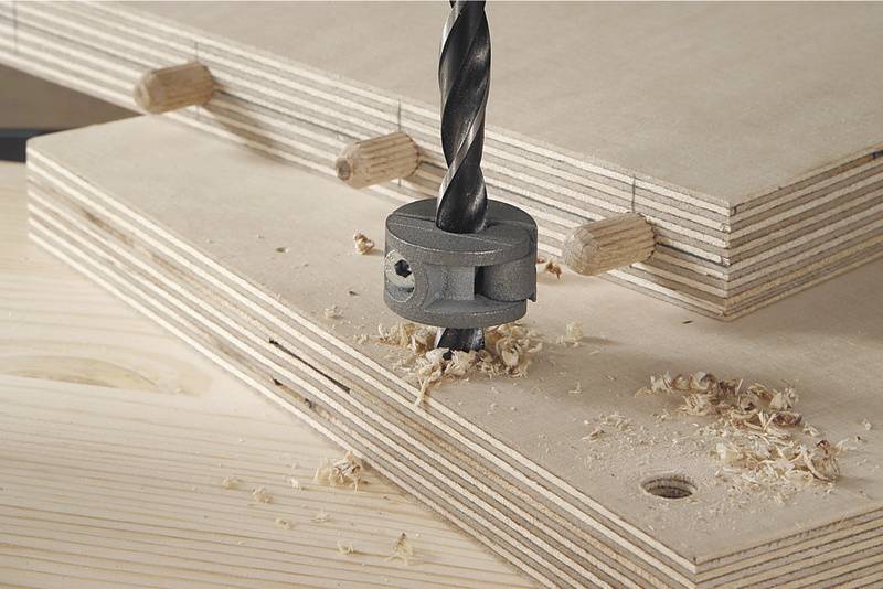 Un foret avec une butée de profondeur perce un trou dans deux planches en bois superposées. Des chevilles sont utilisées pour l'assemblage.
