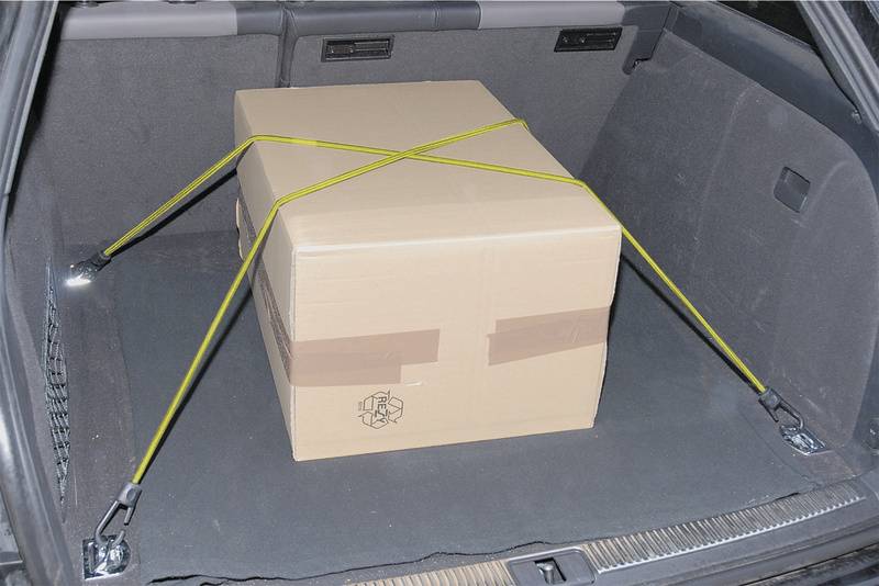 Un grand carton, maintenu par des sangles jaunes, dans le coffre d'une voiture.