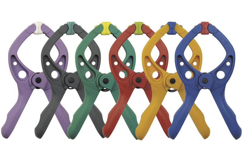Six pinces à ressort de différentes couleurs (violet, gris, vert, rouge, jaune) disposées en ligne.