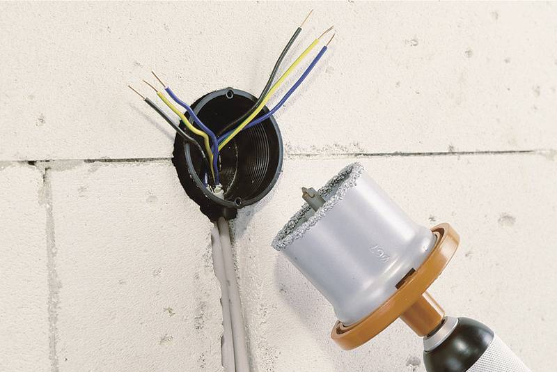 Installation électrique : Un mur est percé à l'aide d'un scie-cloche pour créer une ouverture circulaire destinée aux câbles électriques.