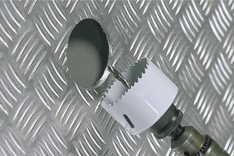 Un cercle est percé dans une tôle nervurée en aluminium. Une scie-cloche est fixée à la perceuse.