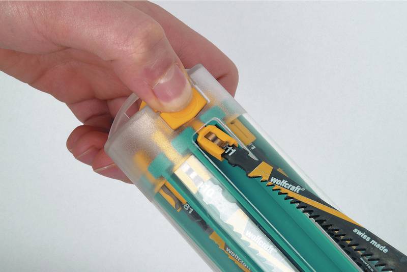 Une main ouvre un emballage en plastique contenant différentes lames de scie. Les lames de scie sont conservées dans un tube transparent.