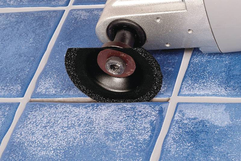 Une machine électrique à couper les carreaux coupe une dalle de céramique bleue. La lame se déplace le long d'une ligne de carrelage.