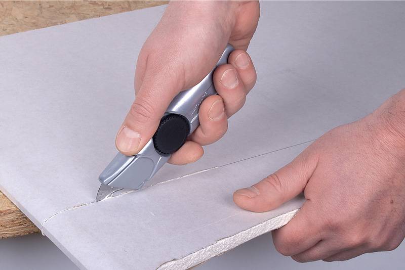 Une personne coupe une plaque de plâtre avec un cutter.