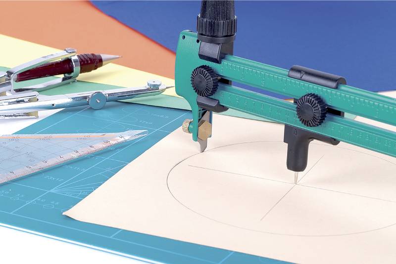 Un compas trace un cercle sur du papier, entouré de règles et d'un crayon sur un tapis de coupe bleu.