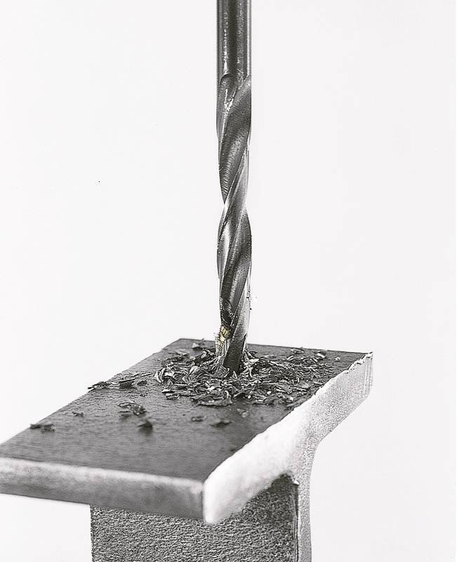 Un foret perfore un morceau de métal. Des copeaux métalliques sont dispersés sur la surface.