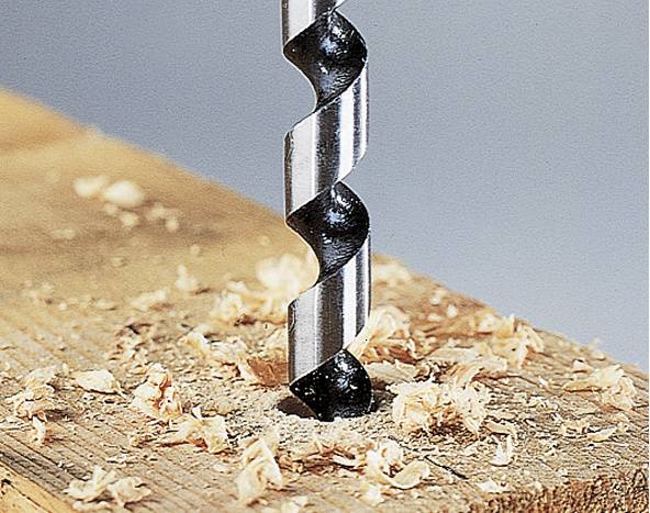 Un foret hélicoïdal perce un trou dans un morceau de bois, entouré de copeaux de bois.