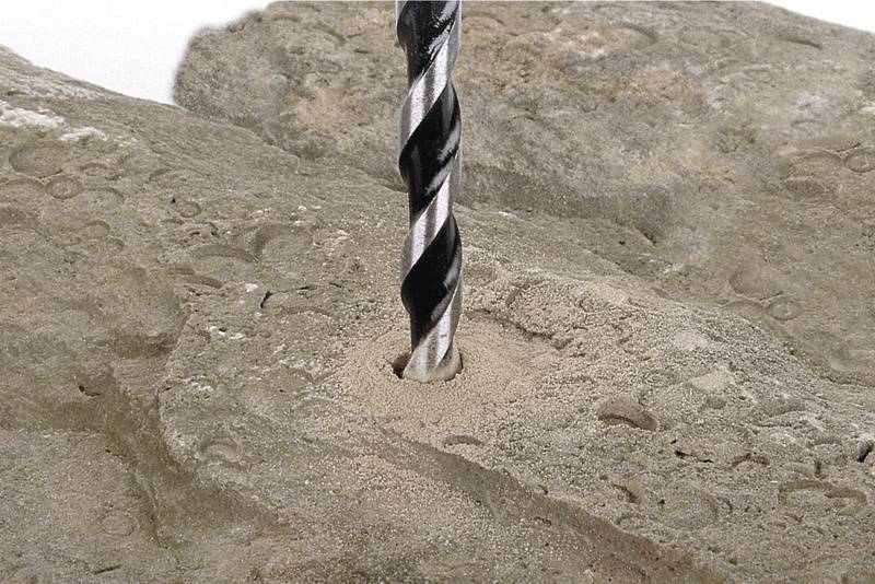 Un foret perfore un bloc de roche. De la poussière s'accumule autour du trou.