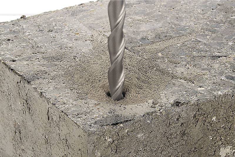 Un foret pénètre dans un bloc de béton et génère de la poussière de perçage autour du trou.