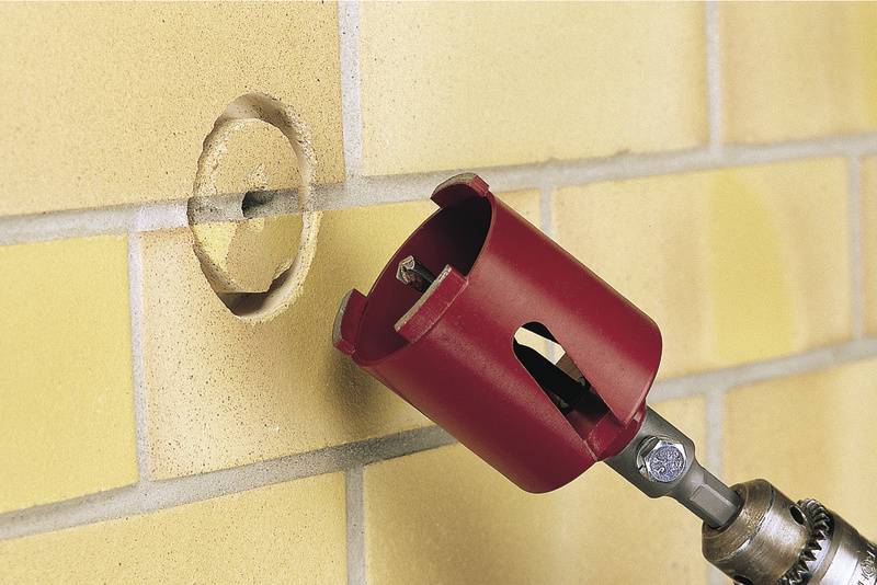 Un foret rouge perce un trou circulaire dans un mur de briques jaunes.