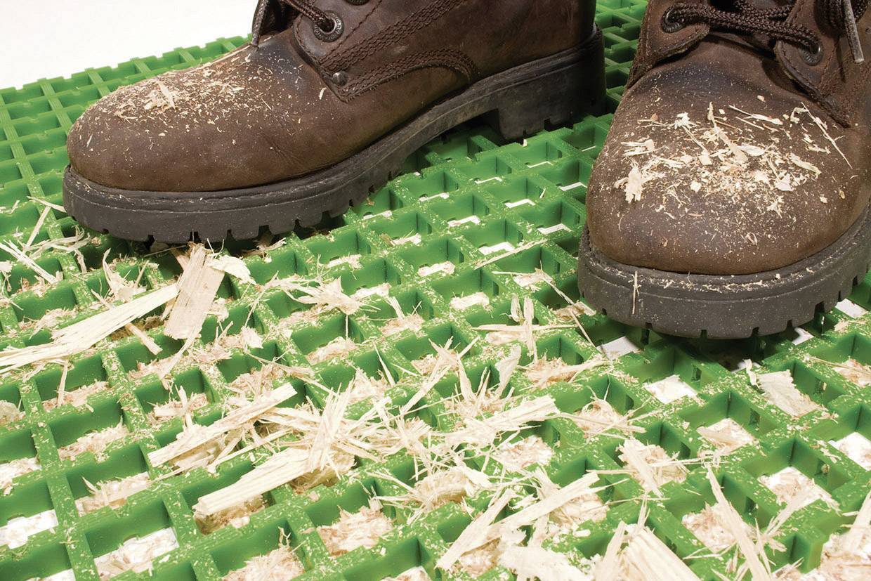 Une paire de bottes brunes est posée sur un tapis de grille vert, recouvert de copeaux de bois.