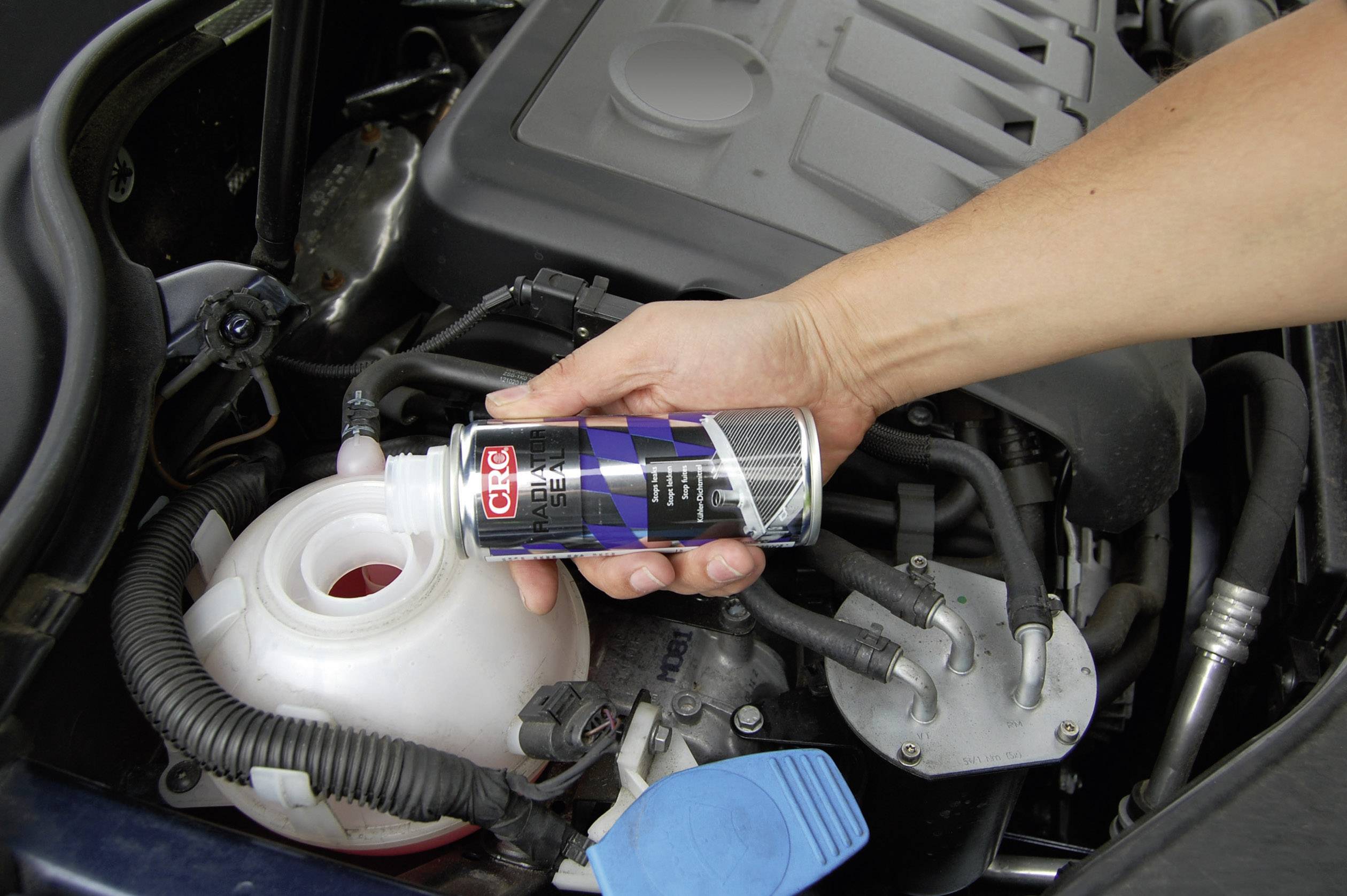 Une main tient une bouteille de liquide de refroidissement et la verse dans le réservoir de liquide de refroidissement d'une voiture afin de protéger le moteur.